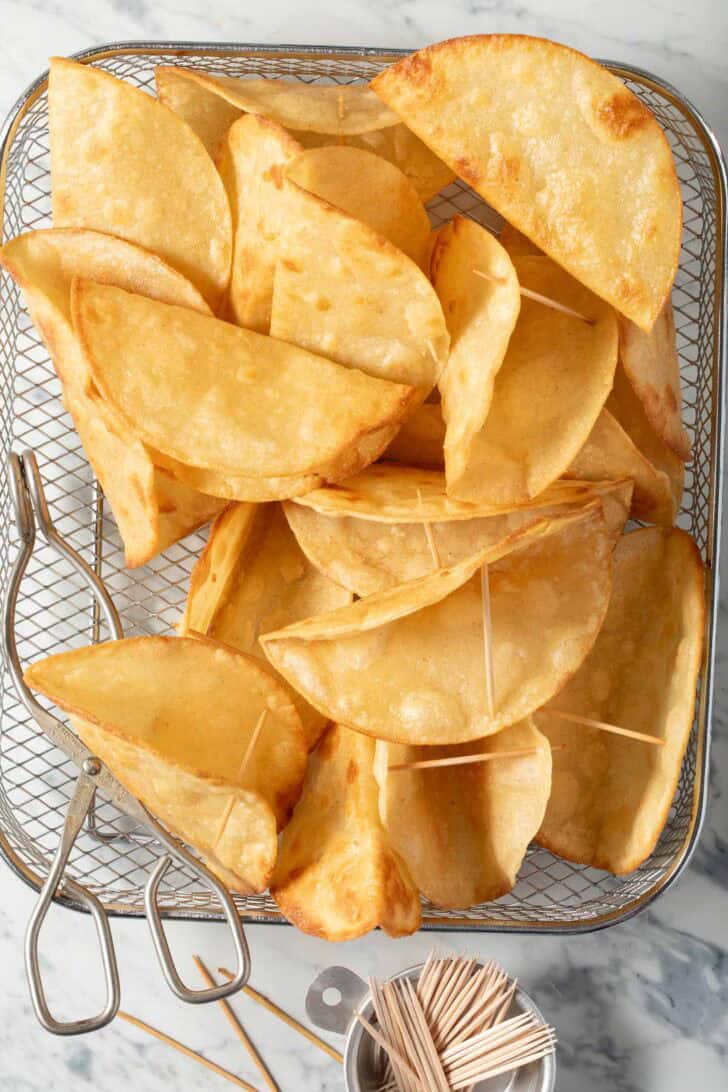 Several homemade crispy taco shells in a wire basket.