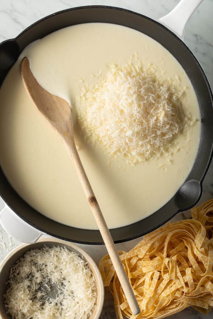 Easy Alfredo Sauce in a pan with a wooden spoon.
