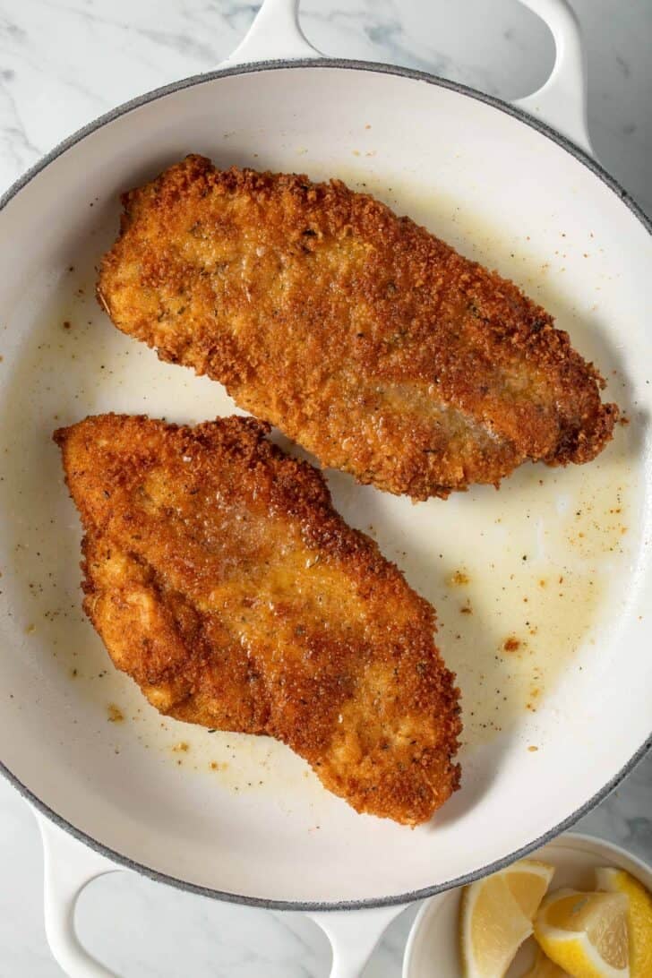 Chicken Milanese cutlets in a white skillet for Chicken Alfredo.