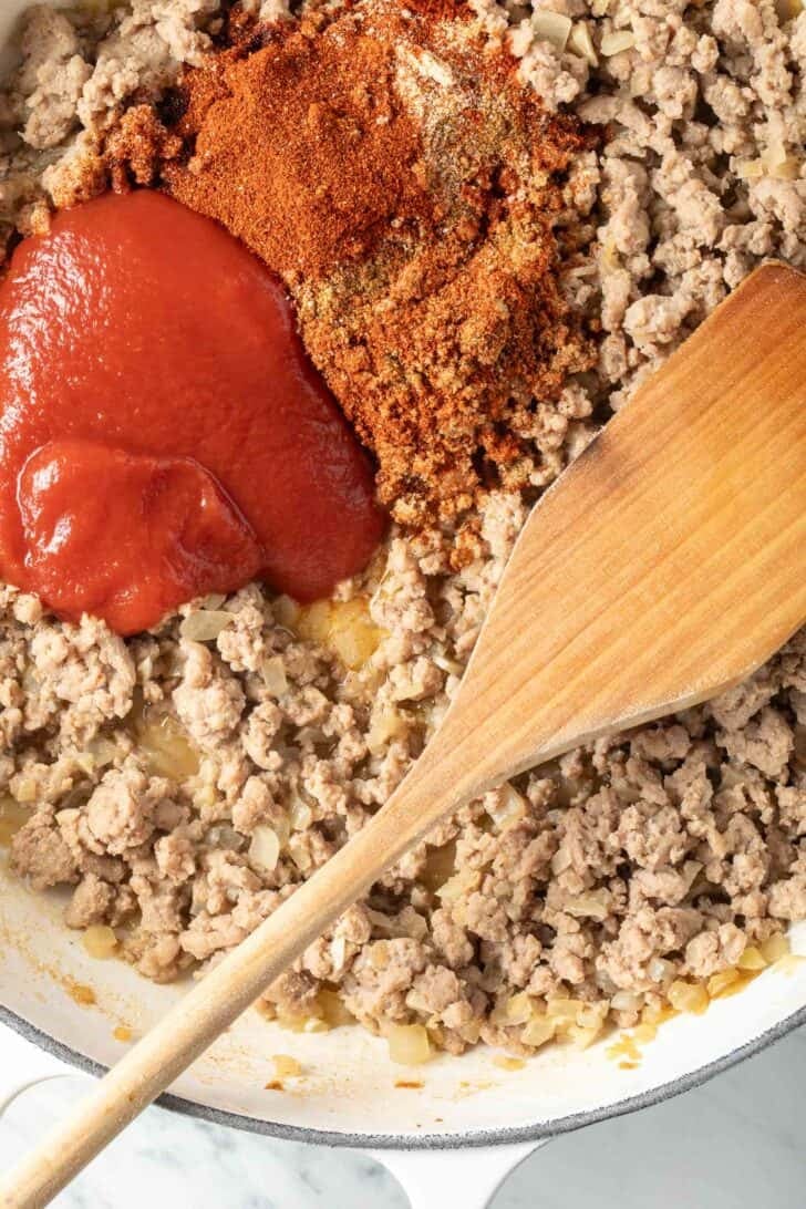 Ground turkey with spices and tomato sauce in a white skillet.