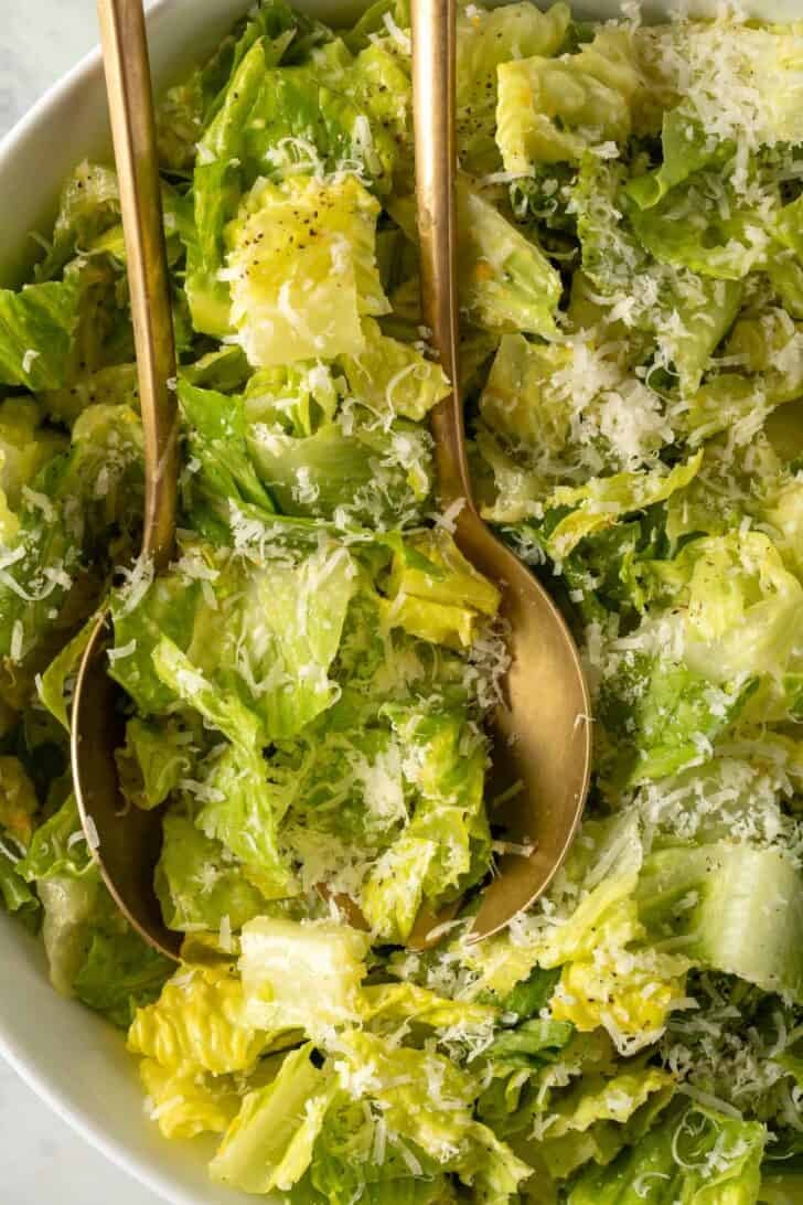 Lemon Parmesan Lettuce Salad in a white bowl with golden salad servers.