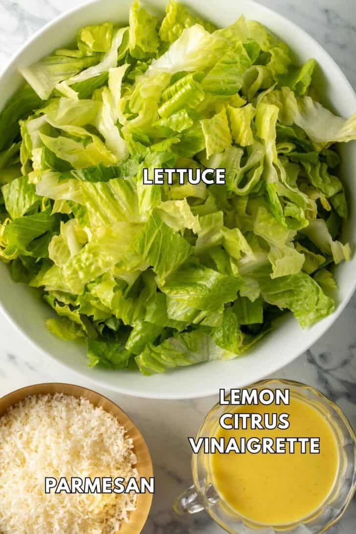 Chopped greens in a white bowl next to a bowl of vinaigrette.