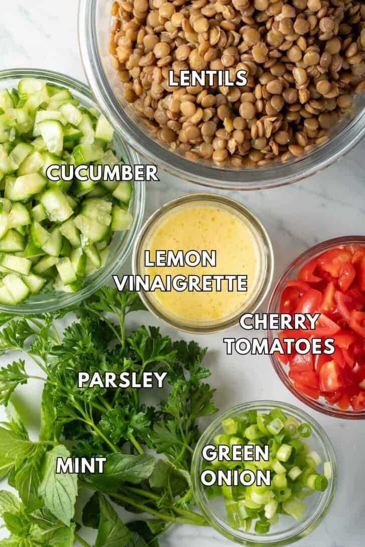 Clear glass bowls filled with green lentils, chopped cucumber, cherry tomatoes, green onion and lemon vinaigrette.