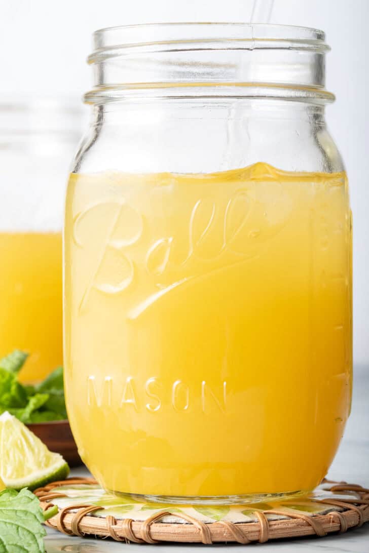 Mango Tea in a clear glass mason jar with a straw.