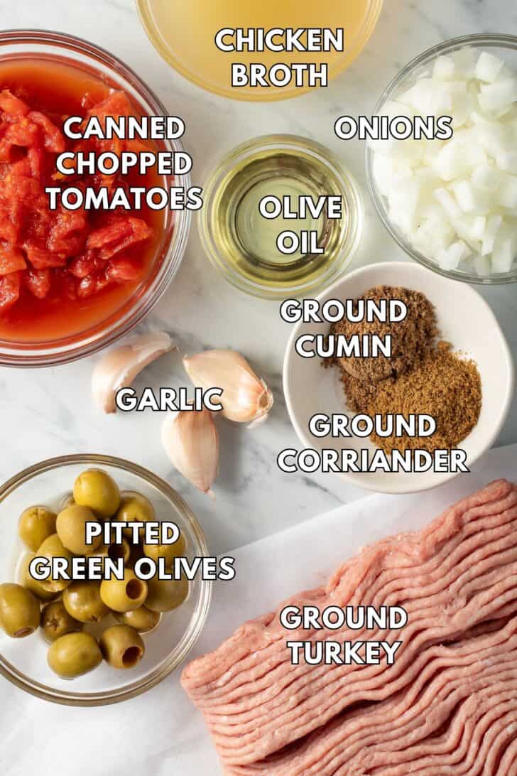 Clear glass bowls filled with green olives, chopped onion, canned tomatoes and chicken broth.
