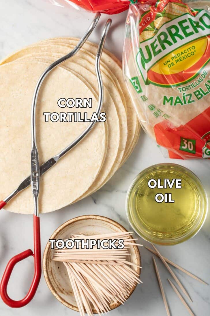 Corn tortillas, olive oil in a glass bowl and toothpick sit next to tongs.