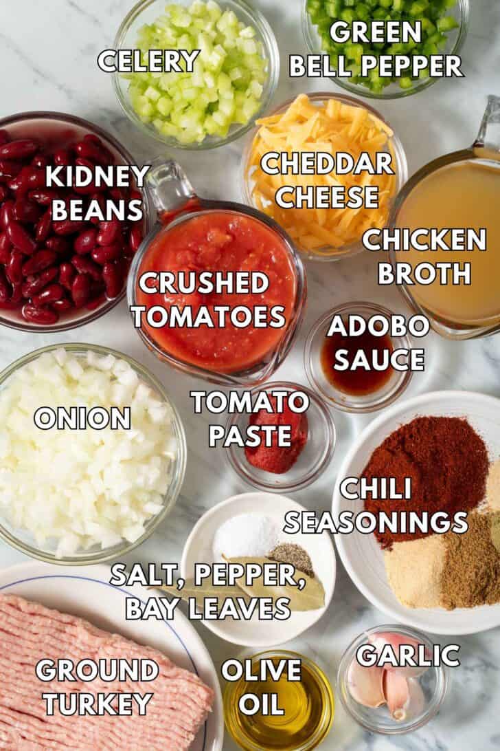 Clear glass bowls filled with kidney beans, crushed tomatoes, chopped onion, grated cheddar cheese, and chicken broth.