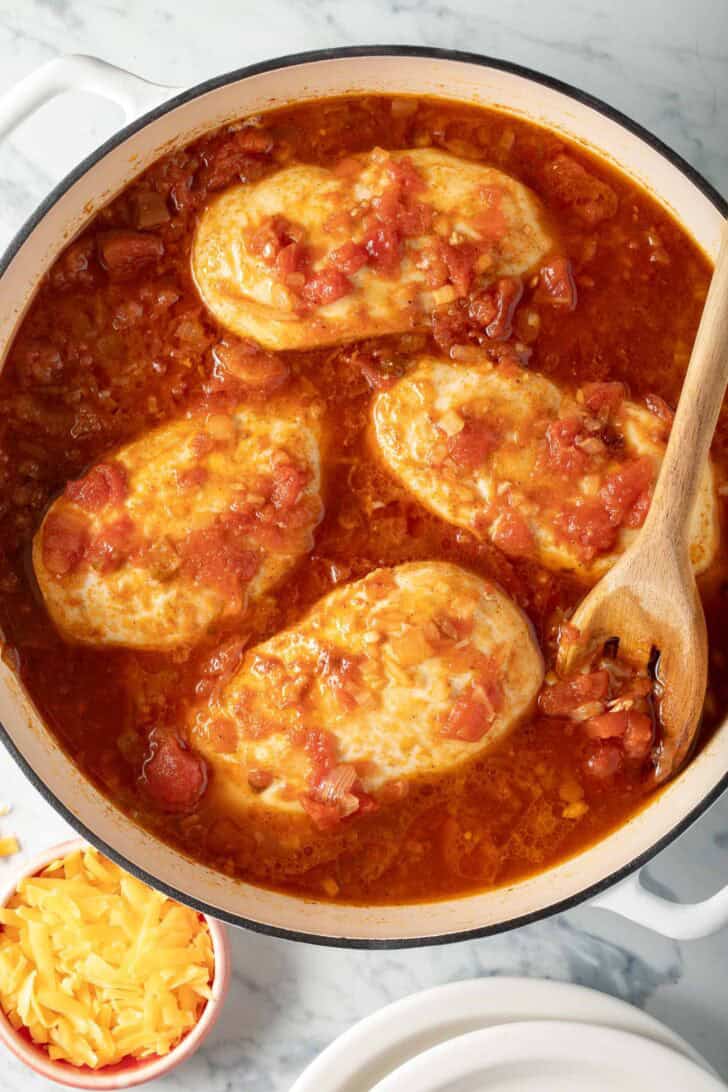 Mexican Shredded Chicken Recipe Chicken breasts simmering in a sauce in a Dutch oven.