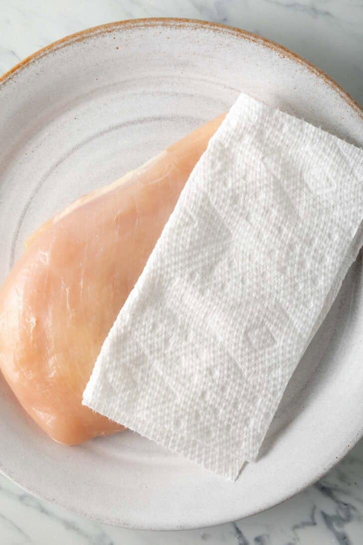 How To Pan Sear Chicken Breast Raw chicken breast on a white plate.