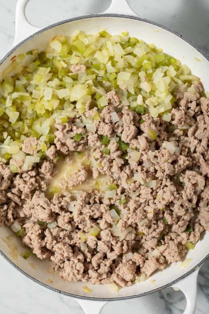 Cooked onion, garlic, celery, bell pepper and ground turkey in a white pot.