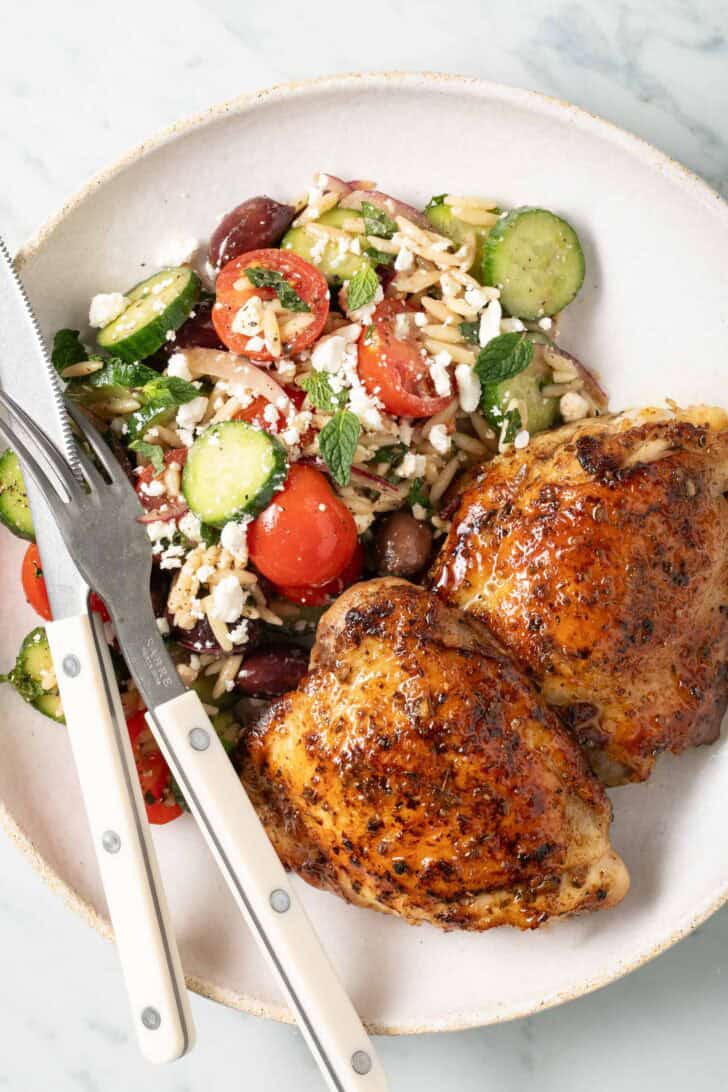 Greek Chicken Thighs Marinated Greek Chicken Thighs on a white plate with a salad.
