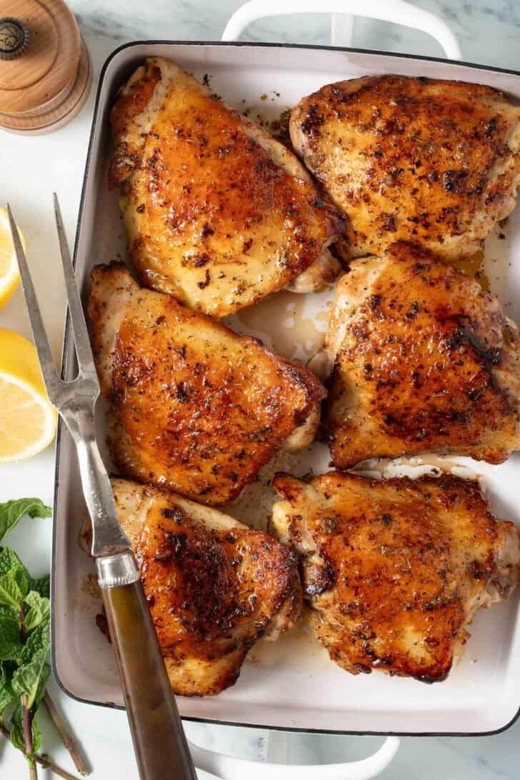 Greek Chicken Thigh Marinade Marinated chicken thighs in a white baking dish.