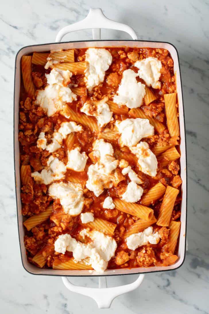 Baked Rigatoni and Ricotta Rigatoni and meat sauce topped with ricotta cheese in a white baking dish.