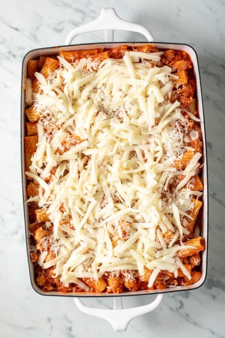 Baked Rigatoni with Sausage Rigatoni and sausage meat sauce with grated mozzarella cheese on top in a white baking dish.