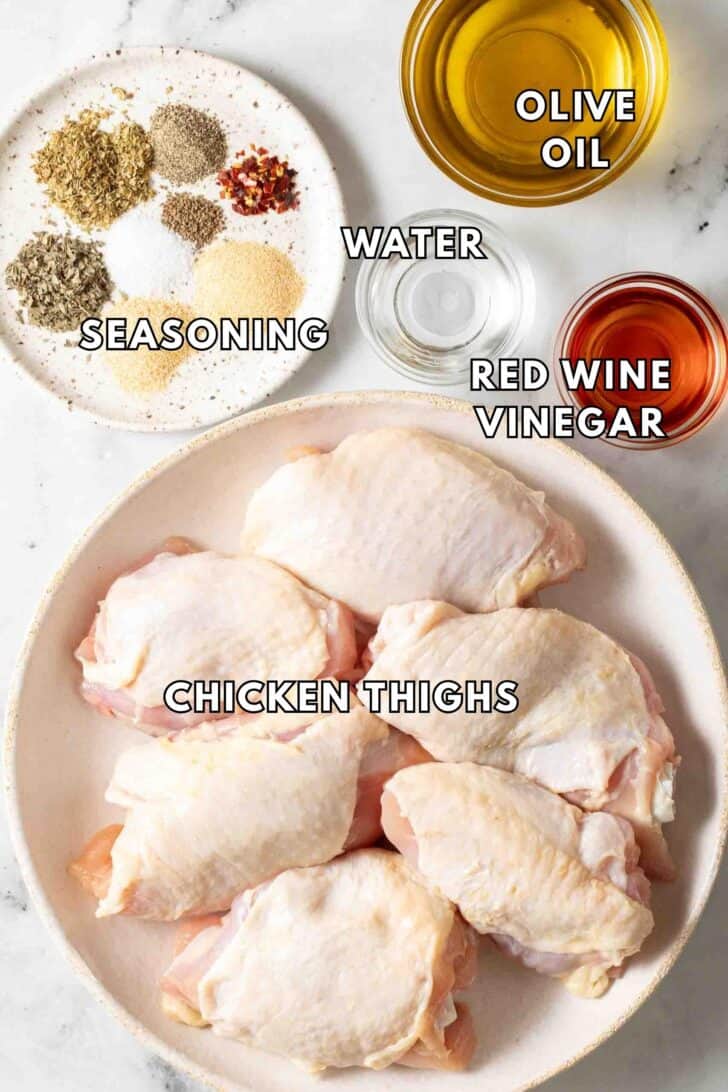 Italian Dressing Chicken Recipe Chicken thighs in a white plate next to a dish of seasoning and a small glass bowl of olive oil.