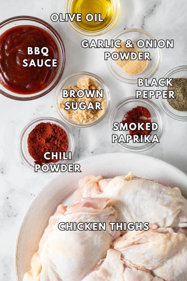 Oven Baked BBQ Chicken Thighs Small glass bowls filled with spices and bbq sauce next to a plate of raw chicken thighs.