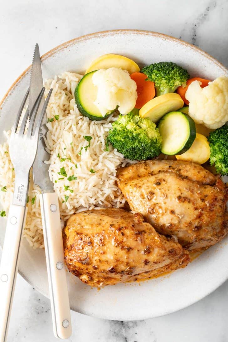 Baking Boneless Skinless Chicken Thighs Baked Boneless Skinless Chicken thighs on a white plate with vegetables and rice.