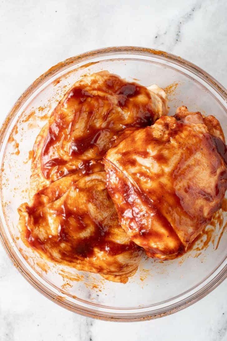 Baked BBQ Chicken Thighs Chicken thighs rubbed with bbq sauce in a clear glass bowl.
