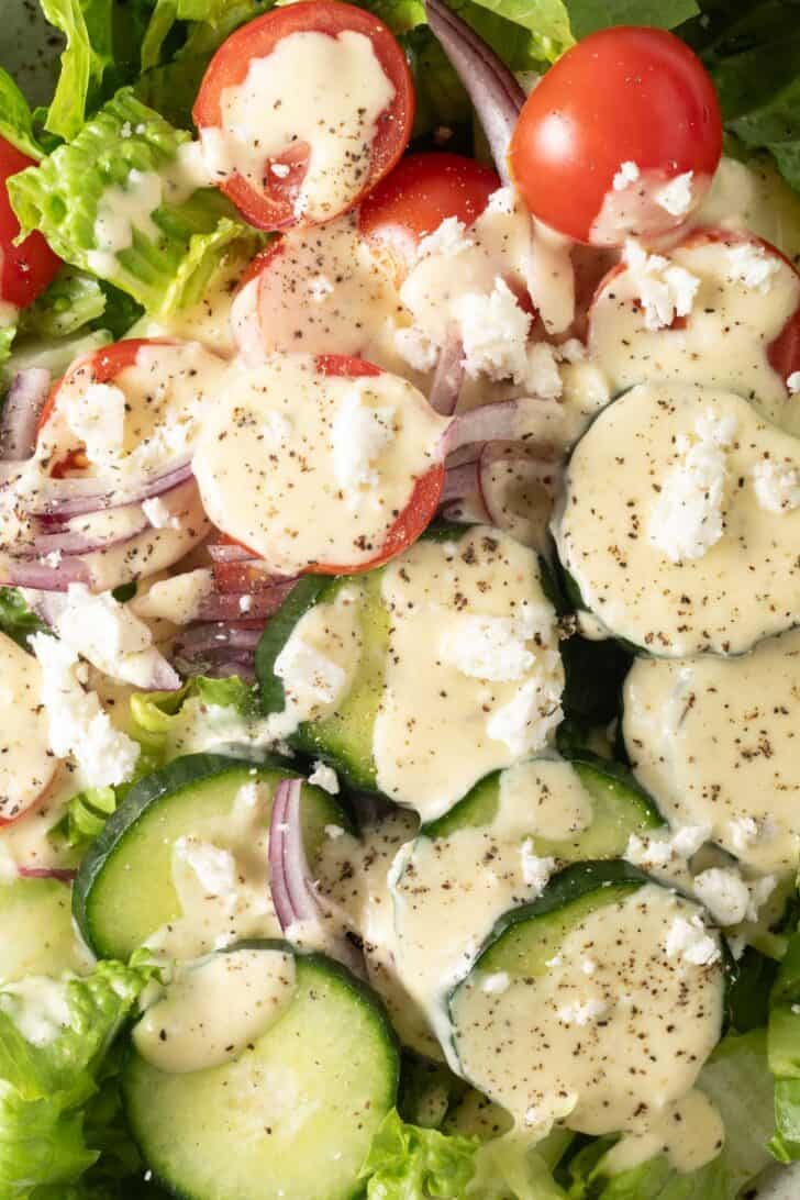 Creamy Greek Dressing Creamy Greek Dressing drizzled over a green salad with cucumbers.