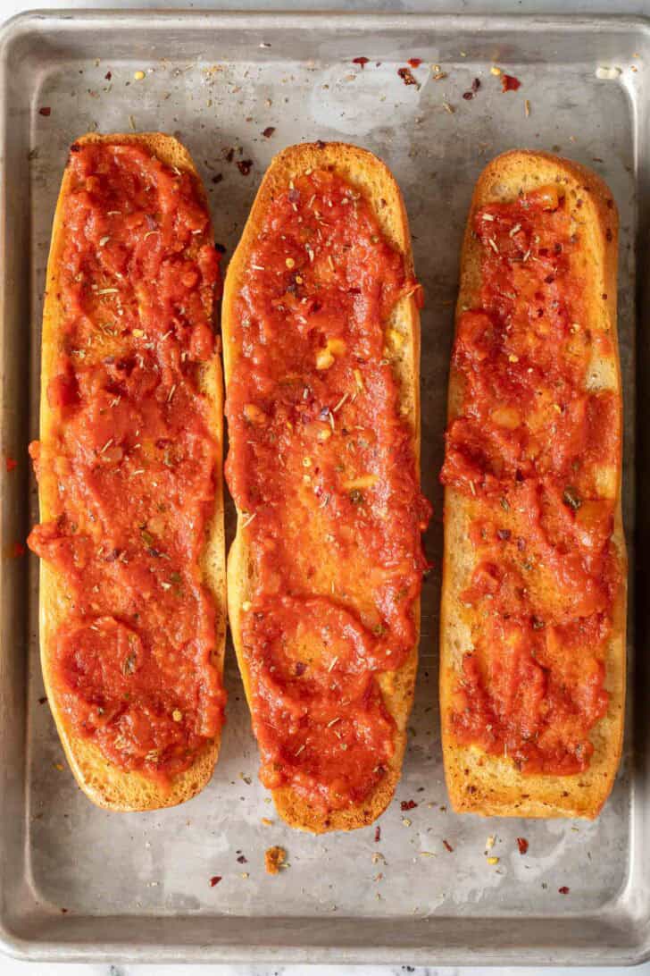 French Bread Pizzas Three half loaves of French bread with marinara sauce spread on them for French Bread Pizzas.