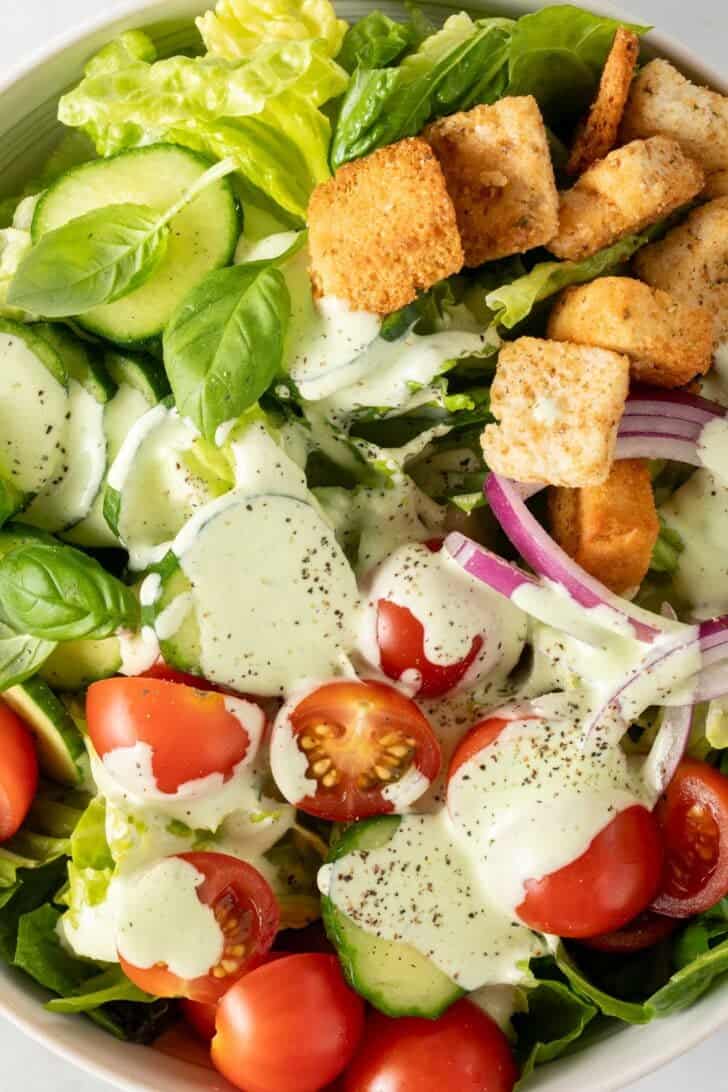 Pesto Ranch Dressing tossed in a green salad in a bowl.