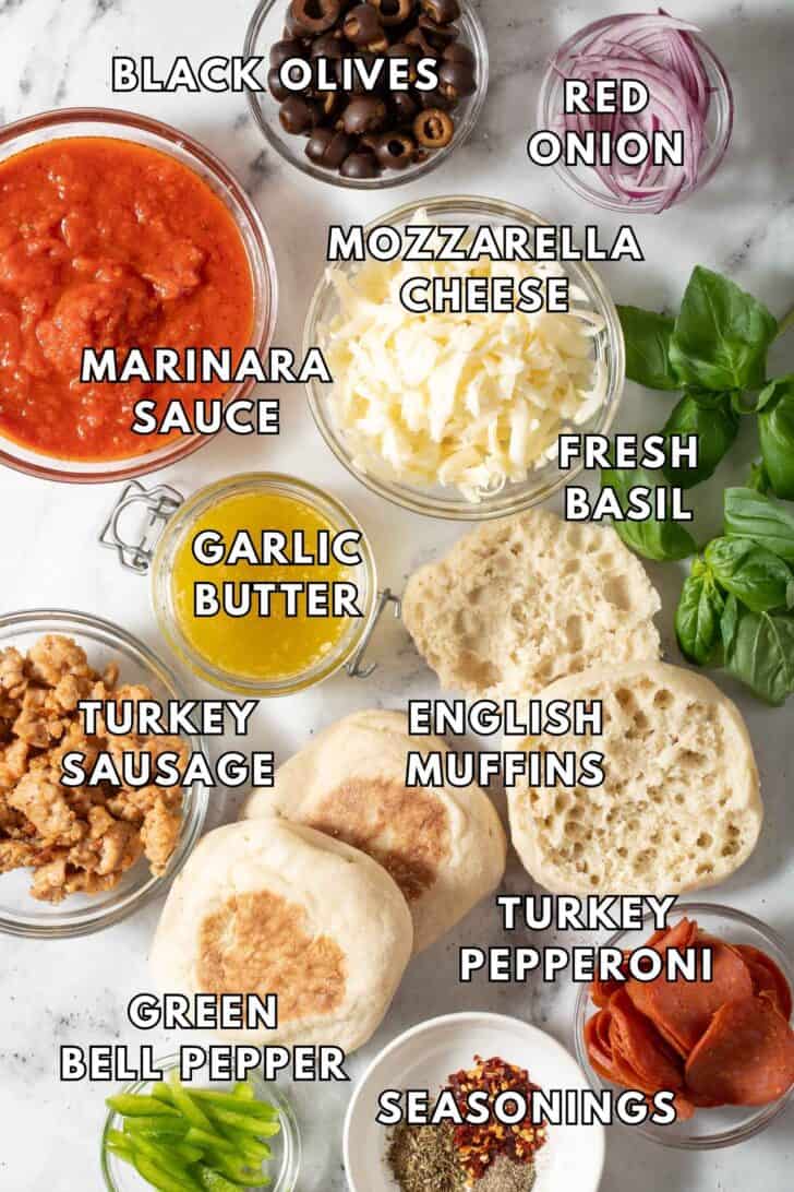 English Muffin Pizza Recipe Clear glass bowls filled with marinara sauce, grated cheese, pepperoni and Italian sausage next to english muffins for English Muffin Pizza recipe.