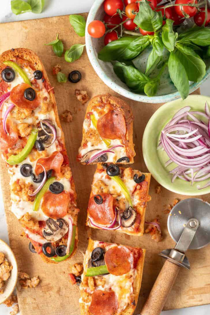 French Bread Pizzas Two French Bread Pizzas on a wood cutting board.