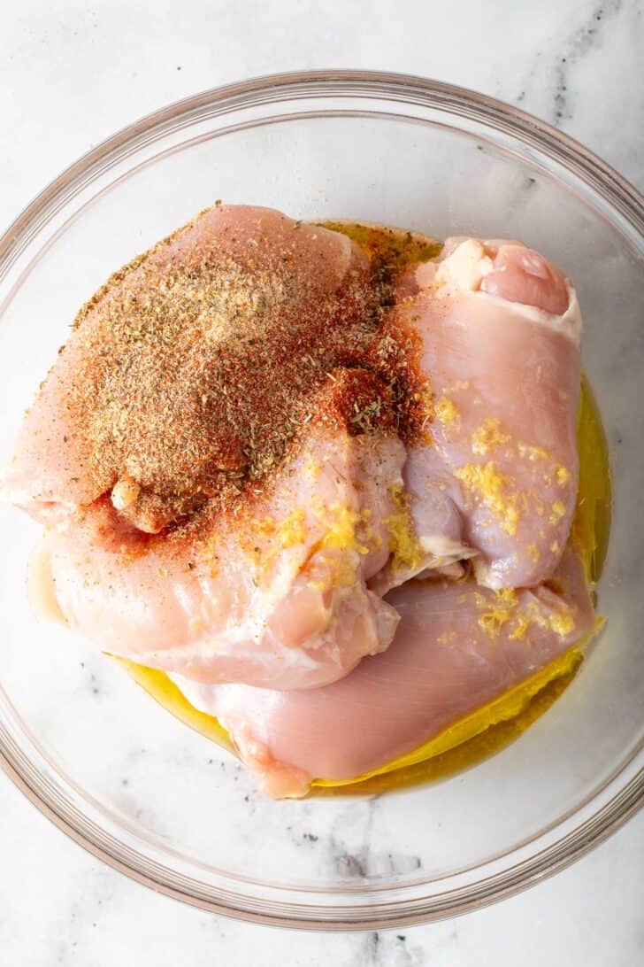 Boneless Skinless Chicken Thighs Raw boneless skinless chicken thighs with seasonings in a clear glass bowl.