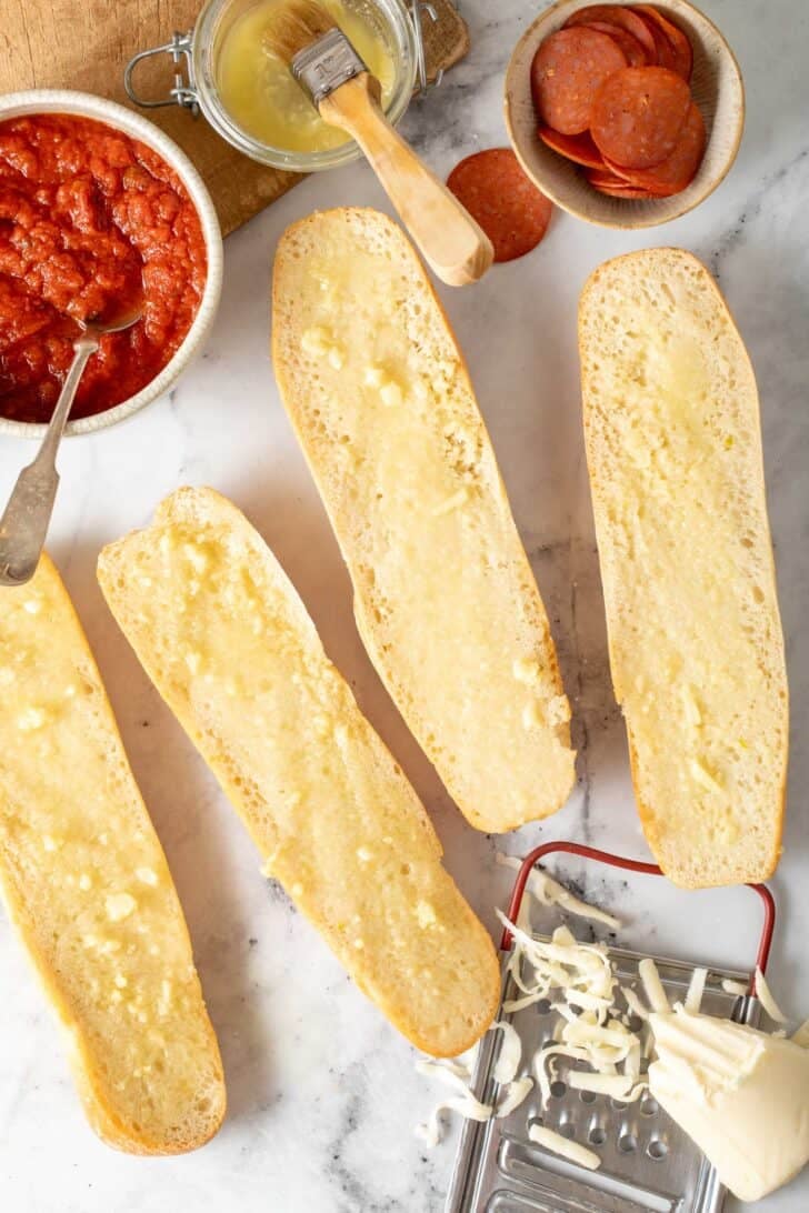 How to Make Garlic Bread Pizza Italian bread loaves sliced in half with garlic butter spread on them.