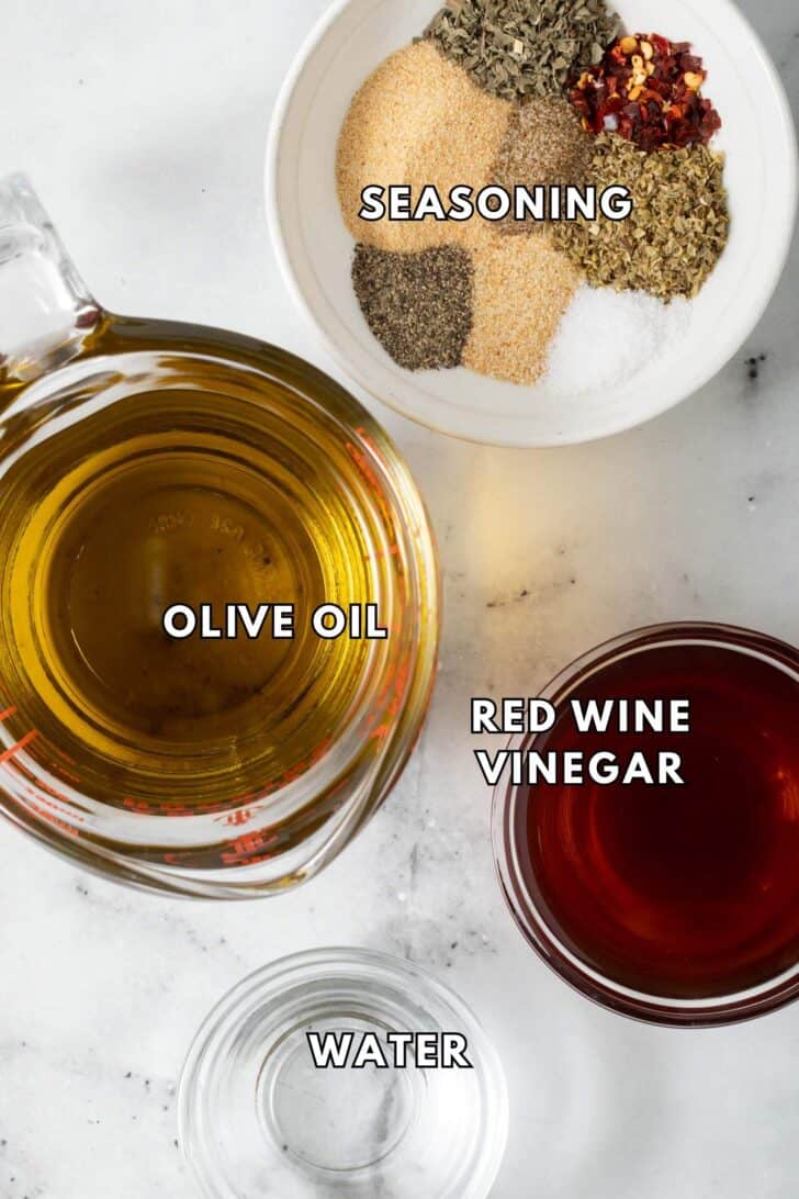 Italian Salad Dressing Recipe Olive oil in a glass measuring cup next to a white dish filled with seasonings.