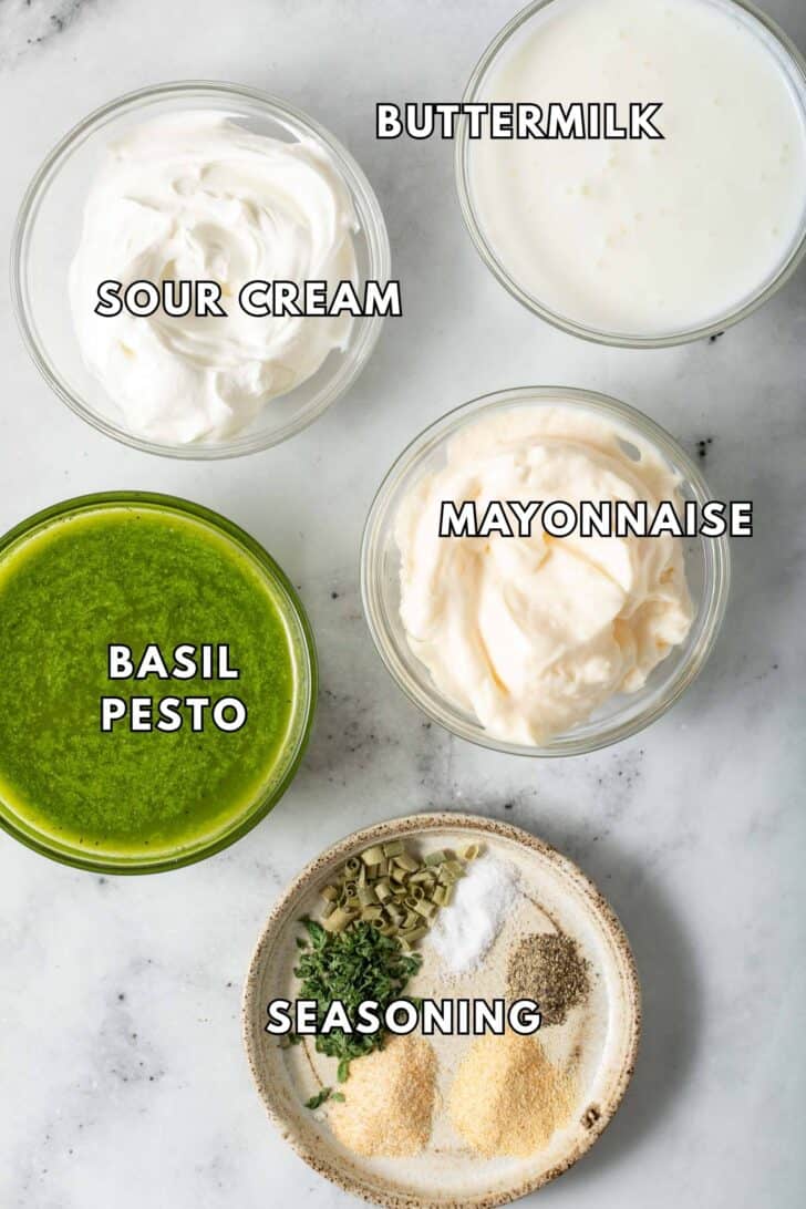 Clear glass bowls filled with basil pesto, sour cream, mayonnaise and buttermilk for pesto ranch dressing recipe.