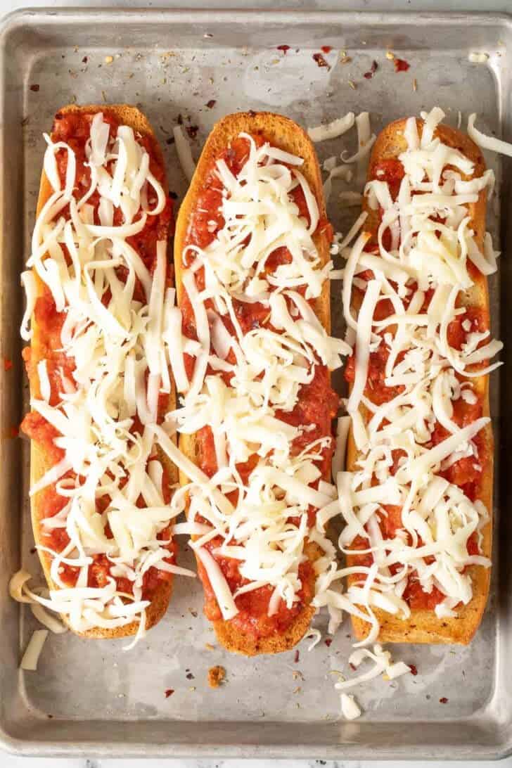 French Bread Pizzas Three half Italian bread loaves with marinara sauce and grated cheese on them for French Bread Pizzas.