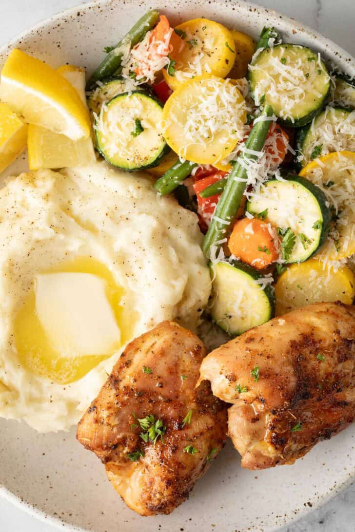 Air Fryer Chicken Thighs on a plate with mashed potatoes and vegetables.