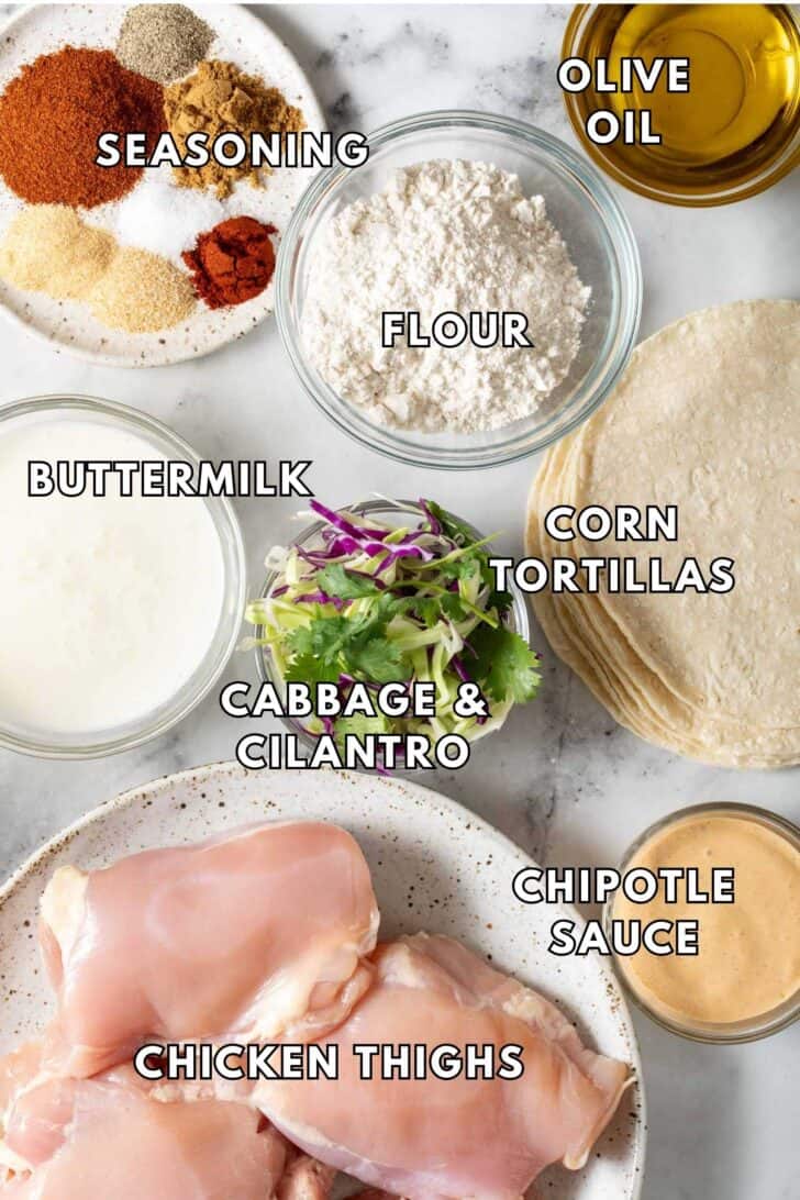 Fried Chicken Tacos Recipe Clear glass bowls filled with buttermilk, all-purpose flour, and seasoning next to a plate of chicken thighs.