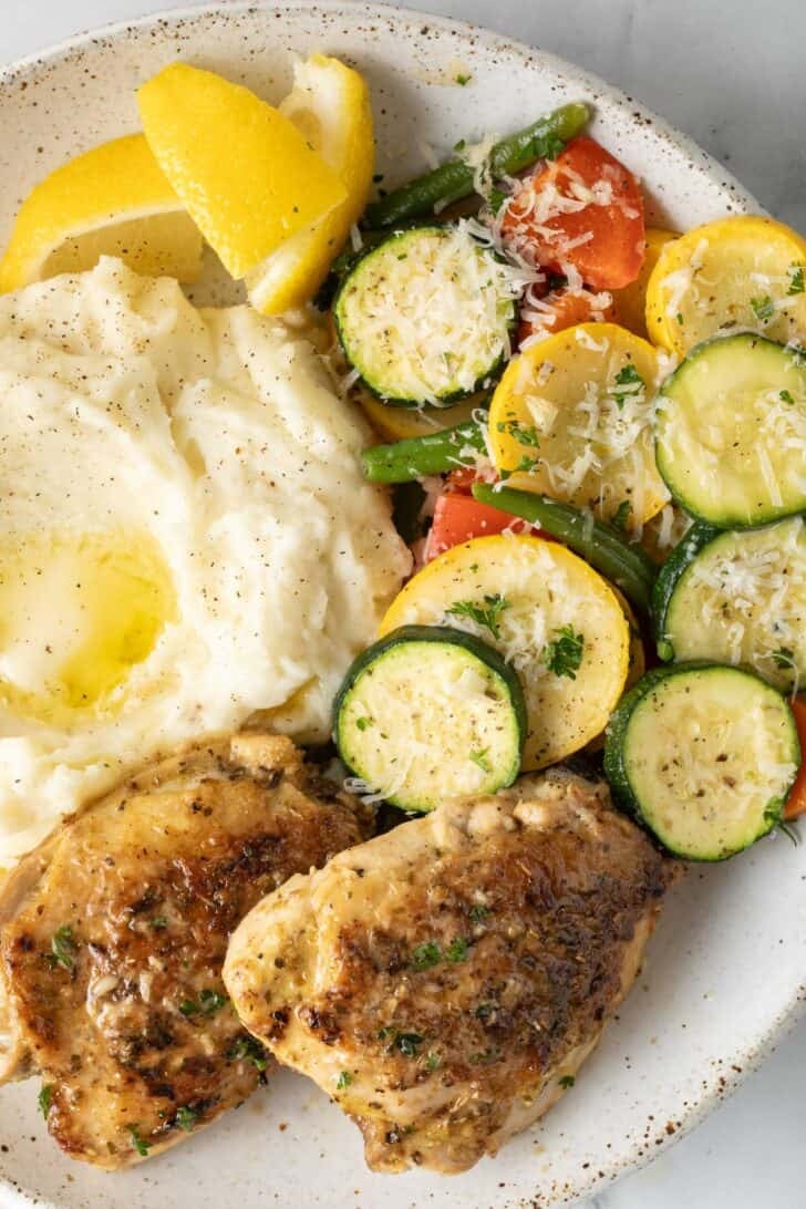 Baked Greek Lemon Chicken Thighs Baked Greek Lemon Chicken thighs on a plate with mashed potatoes and vegetables.