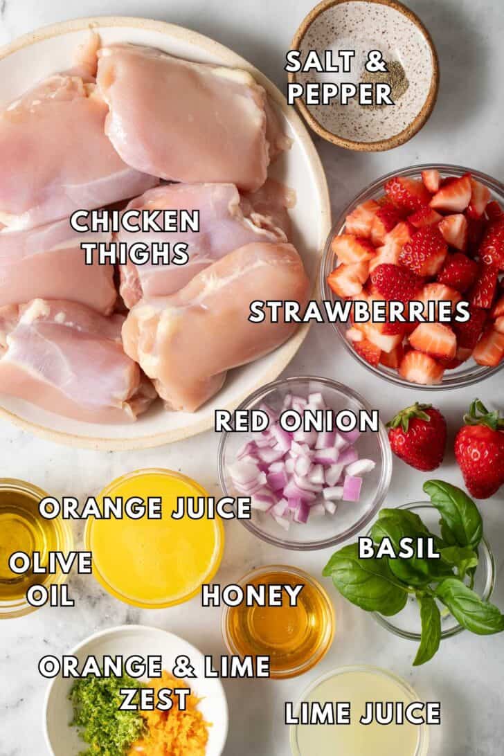 Citrus Marinated Chicken Chicken thighs on a plate nex to bowls of strawberries, onion, and basil.