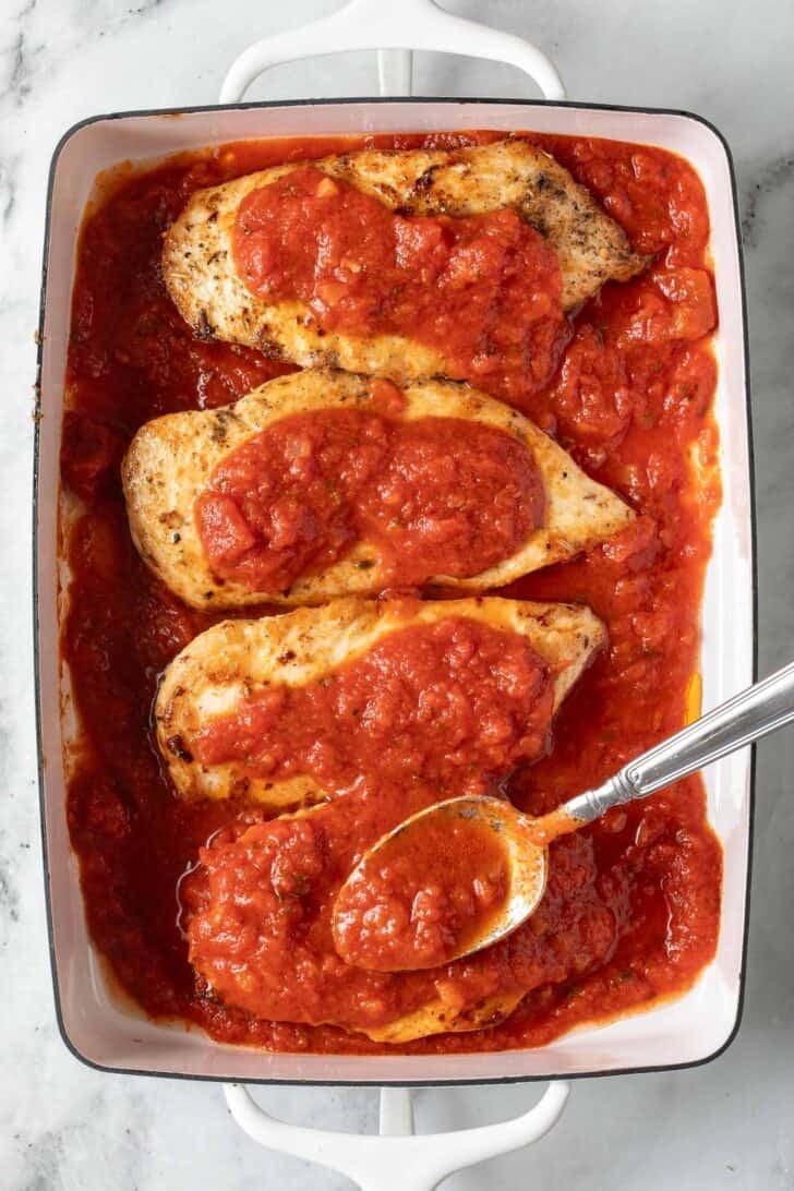 Pizza Baked Chicken Recipe 4 chicken cutlets with marinara sauce in a baking dish.