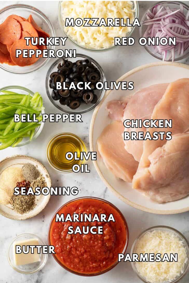 Pizza Bake Chicken Chicken cutlets on a plate next to glass bowls filled with marinara sauce, cheese, turkey pepperoni and olives for a Pizza Bake Chicken recipe.