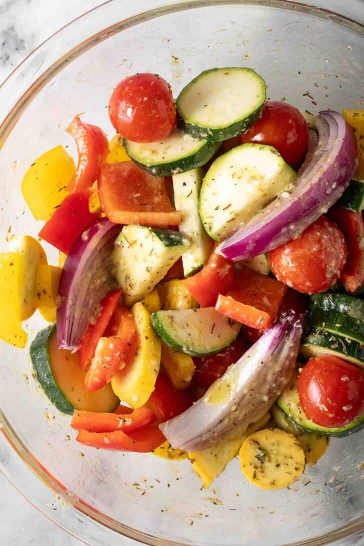 How to Make Greek Sheet Pan Chicken Mixed vegetables tossed with lemon marinade in a clear glass bowl.