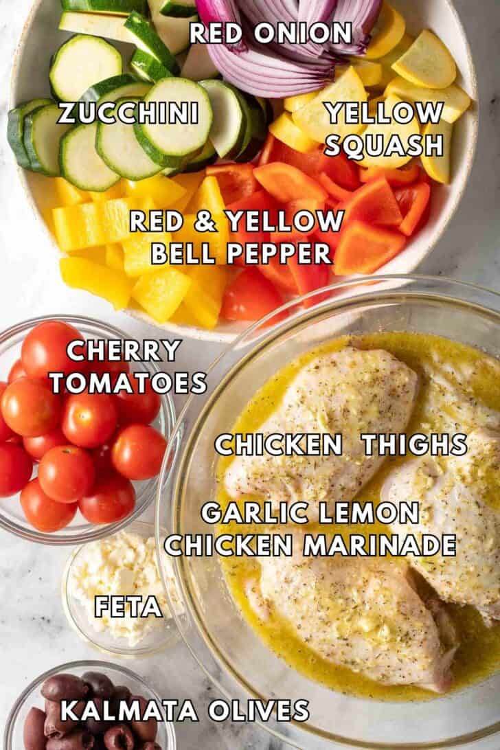 Greek Sheet Pan Chicken Recipe Clear glass bowls filled with marinating chicken, chopped vegetable and cherry tomatoes for Greek Sheet Pan Chicken Recipe
