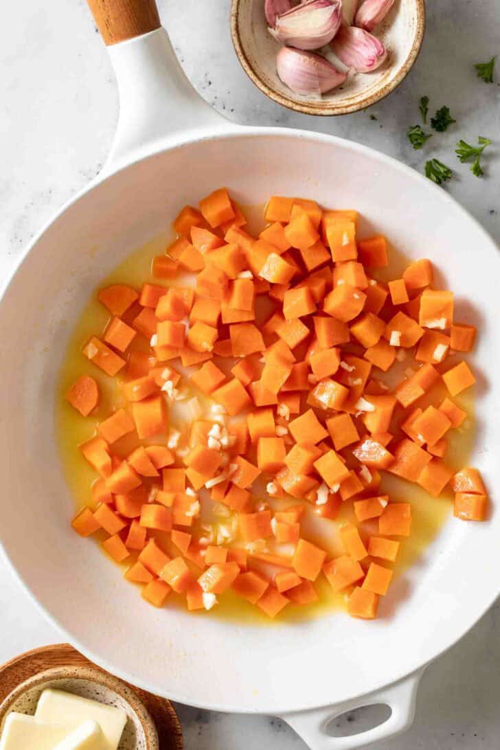 Peas and Carrot Recipe Diced carrots and minced garlic in a white skillet.