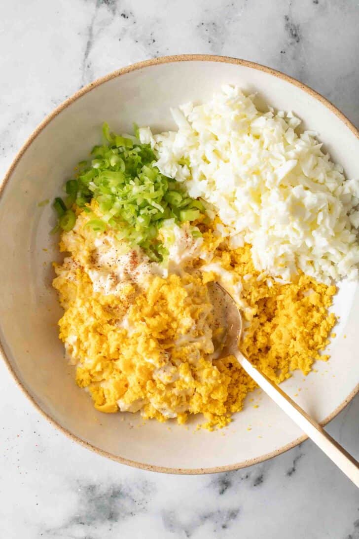 Easy Egg Salad Recipe Mashed hard boiled eggs in a bowl with green onion, Dijon mustard and mayonnaise.