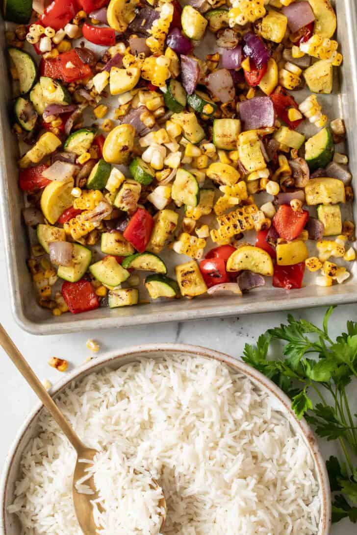 Vegetable Rice Recipe Roasted Vegetables on a sheet pan next to a bowl of basmati rice.
