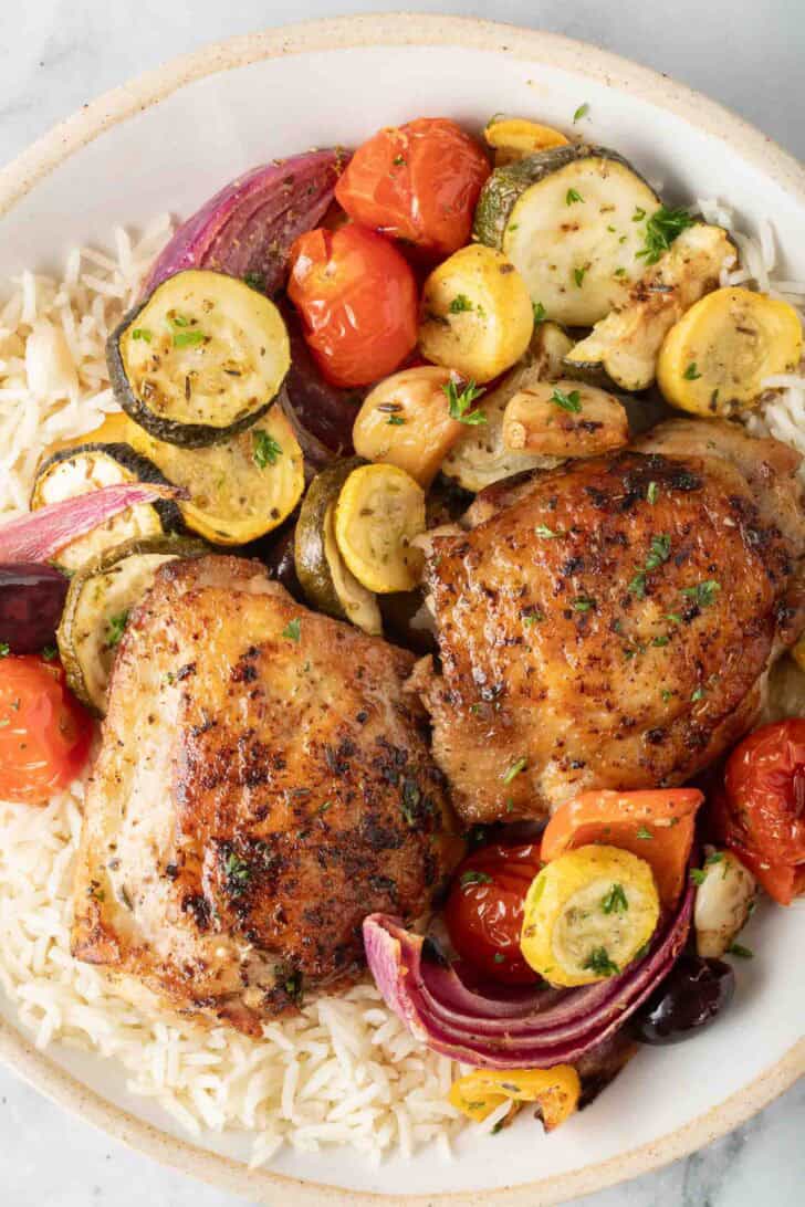 Greek Chicken Sheet Pan Dinner Cooked sheet pan Greek chicken and vegetables on a plate with basmati rice.