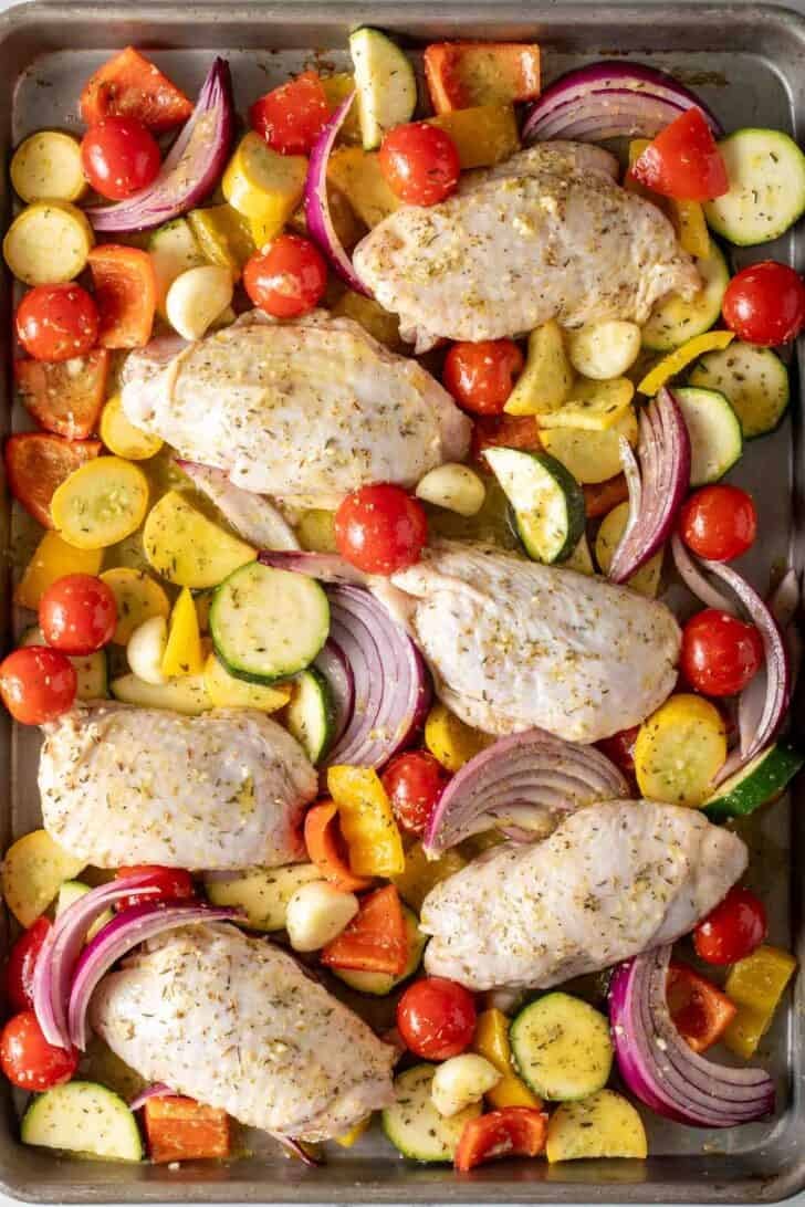 Greek Chicken Sheet Pan Dinner Chicken thighs and sliced vegetables on a sheet pan for Greek Chicken Sheet Pan Dinner