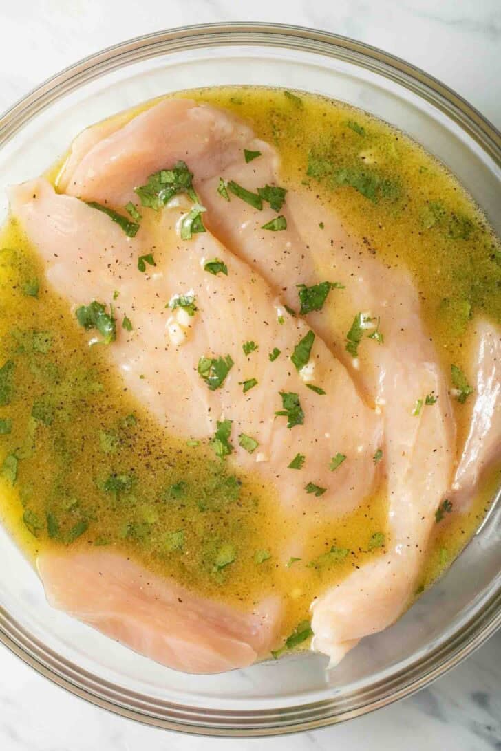 Cilantro Lime Chicken Marinade Raw chicken breasts in a clear glass bowl with cilantro lime chicken marinade.