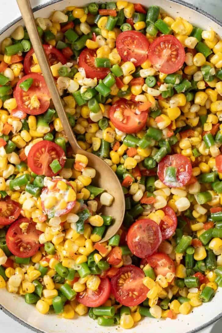 Corn Succotash Corn Succotash in a white skillet with a serving spoon.