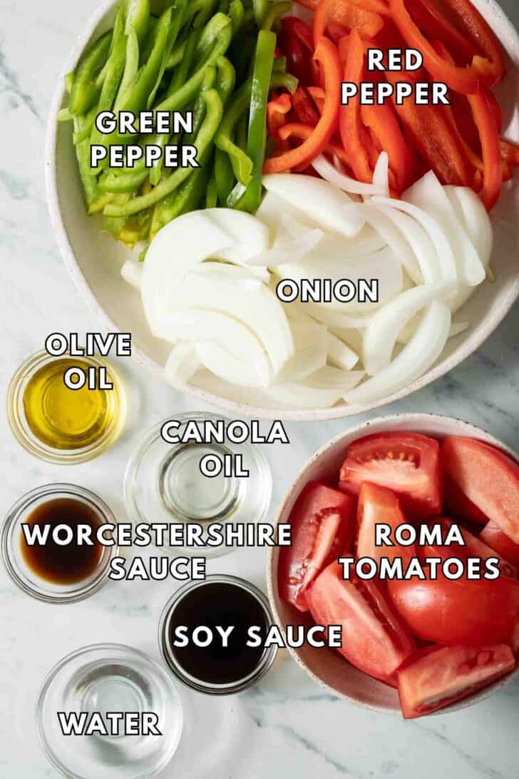 Fajita Veggies Recipe Sliced onion and bell peppers in a bowl next to sliced Roma tomatoes in a bowl for fajita veggies recipe.