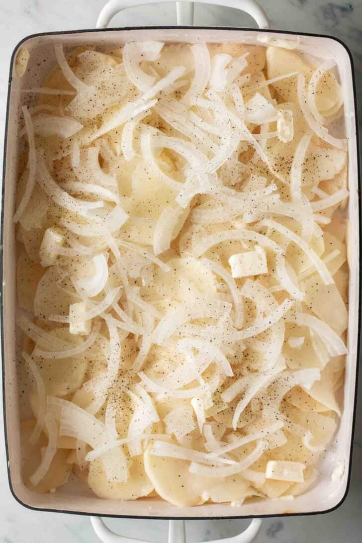 Au Gratin Potatoes Recipe Raw sliced onion and potatoes in a white baking dish for au gratin potatoes recipe.