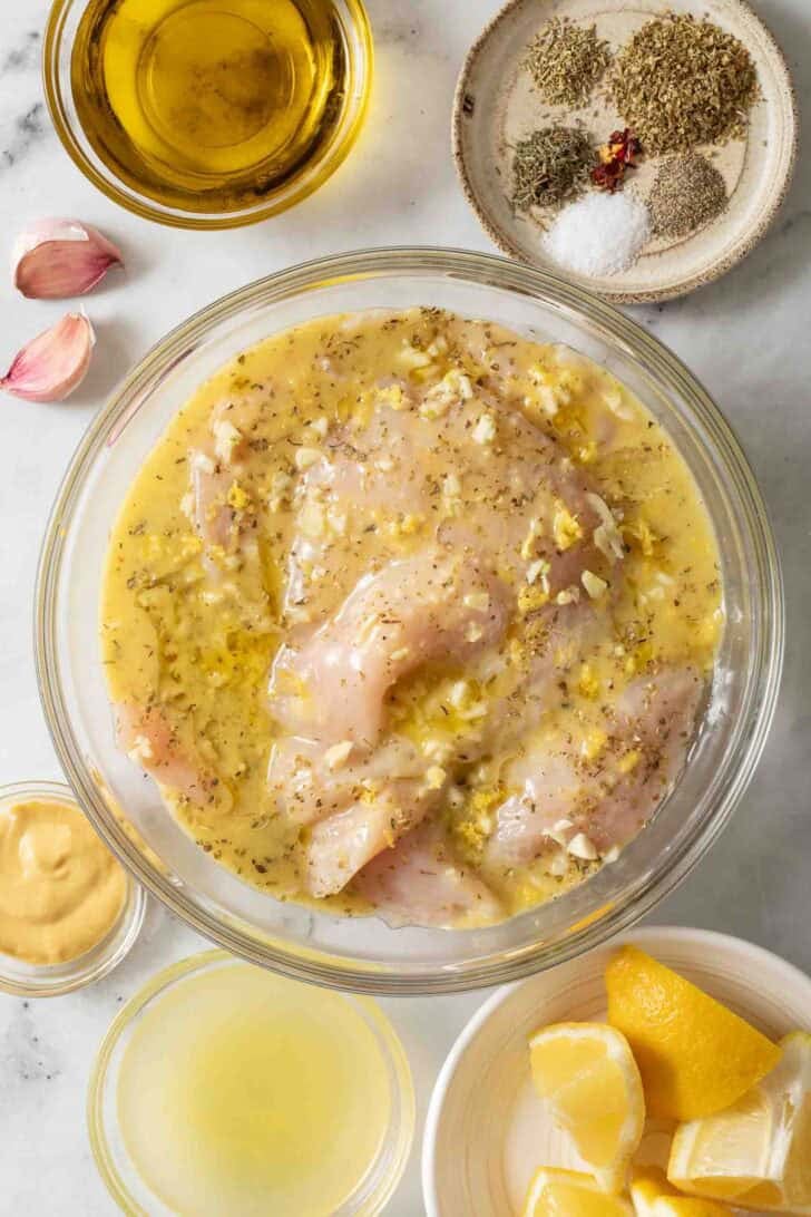 Grilled Lemon Chicken Recipe Chicken marinating in a clear glass bowl.